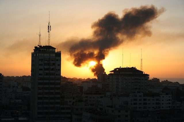 Gaza City Skyline With Smoke A young child sits amid rubble in Gaza, surrounded by destroyed buildings and debris.